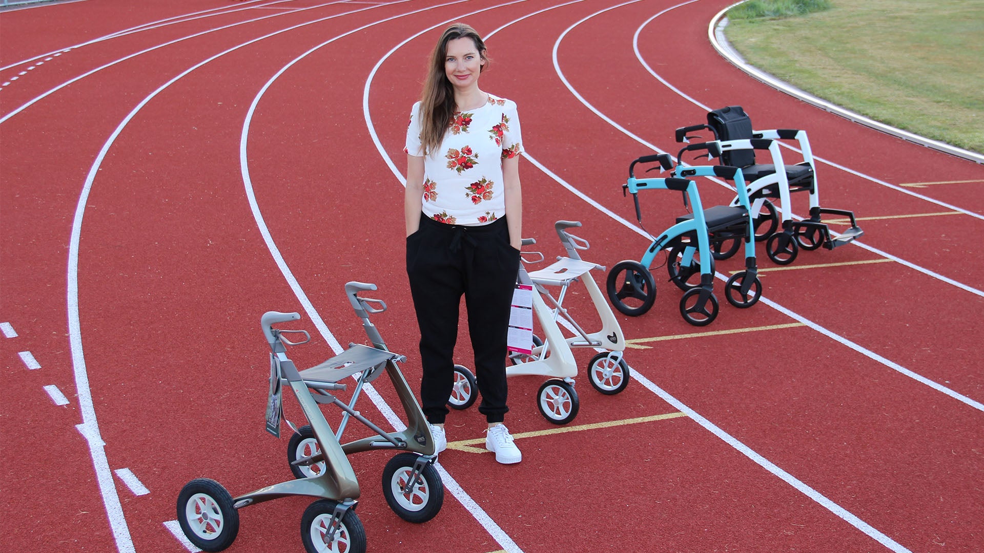 Anna Wallace stands on an athletics track with four different styles of modern walking frames