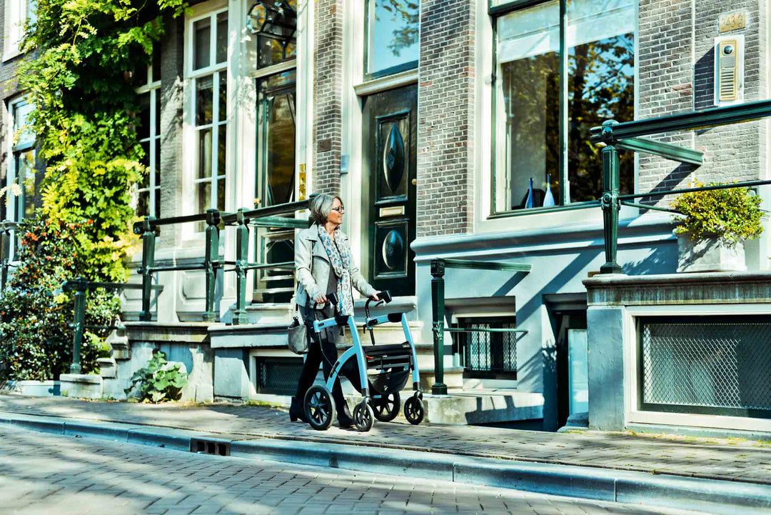 Lady walks along a street beside shops while using a 'Rollz Motion' walking frame