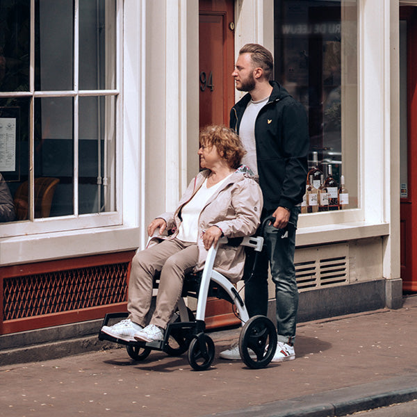 A son pushes his mother in a rollz motion walking frame wheelchair