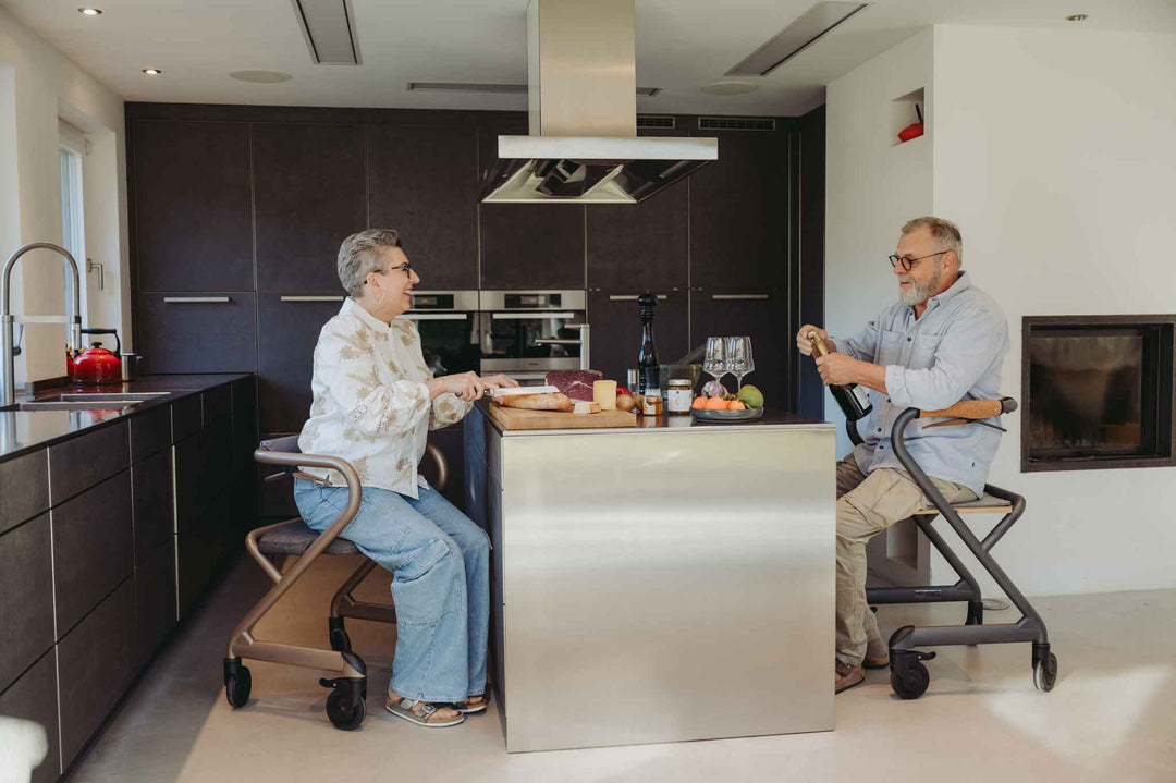 Two people sitting at a kitchen island, both using indoor walkers while preparing lunch in a kitchen