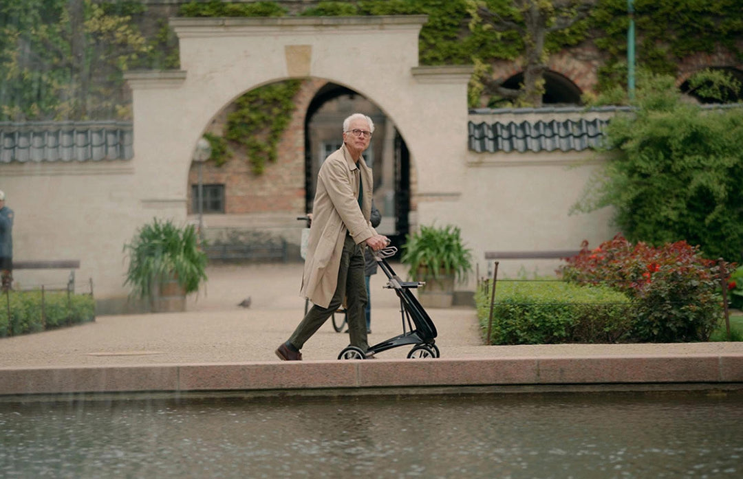 A man walks past a fountain in a courtyard while using a carbon fibre walking frame