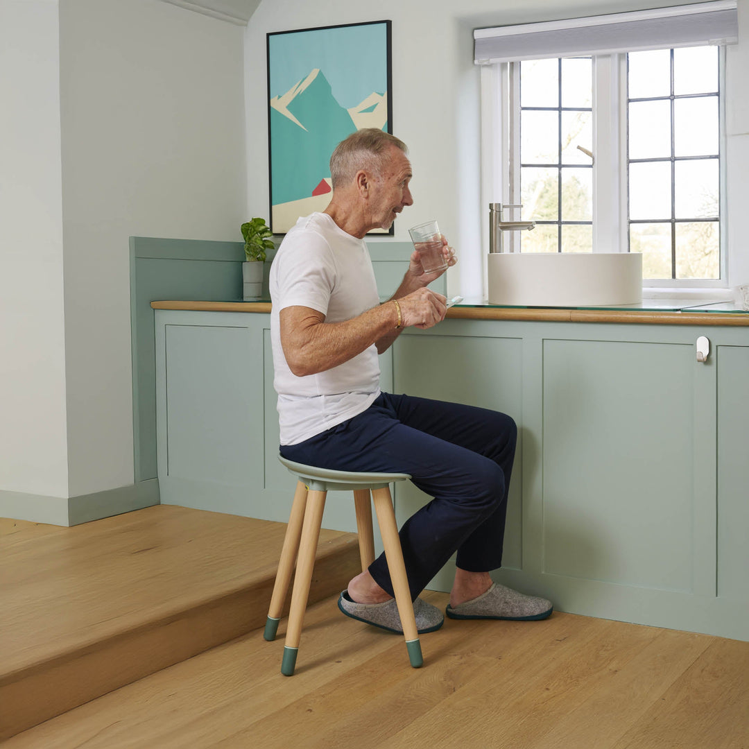 Man sitting on a Spryly Shower Stool in a bathroom, drinking from a glass.