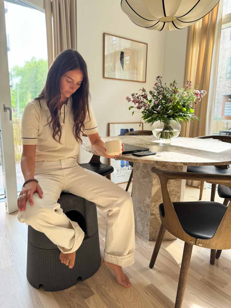 Woman sitting on a black Dorica stool in a modern living room with a dining table and decor.