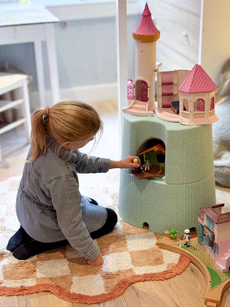 Child playing with a toy castle set on a wooden floor.