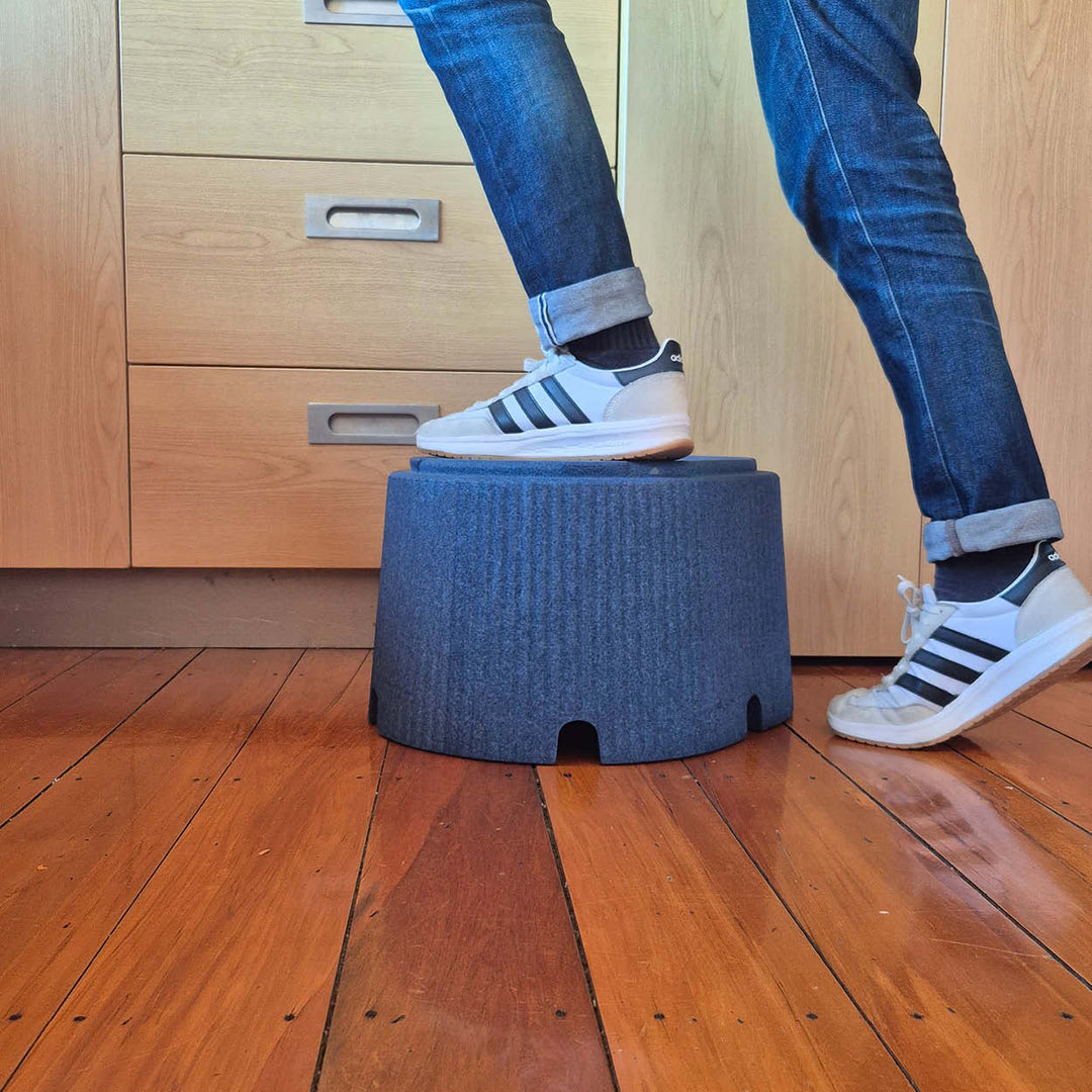 Person stepping onto a small blue step stool on a wooden floor.