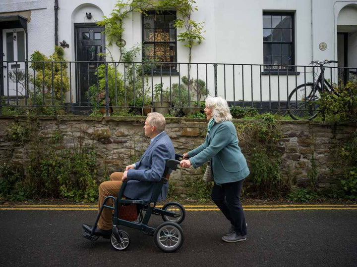 Woman pushing a man in a wheelchair on a residential street.