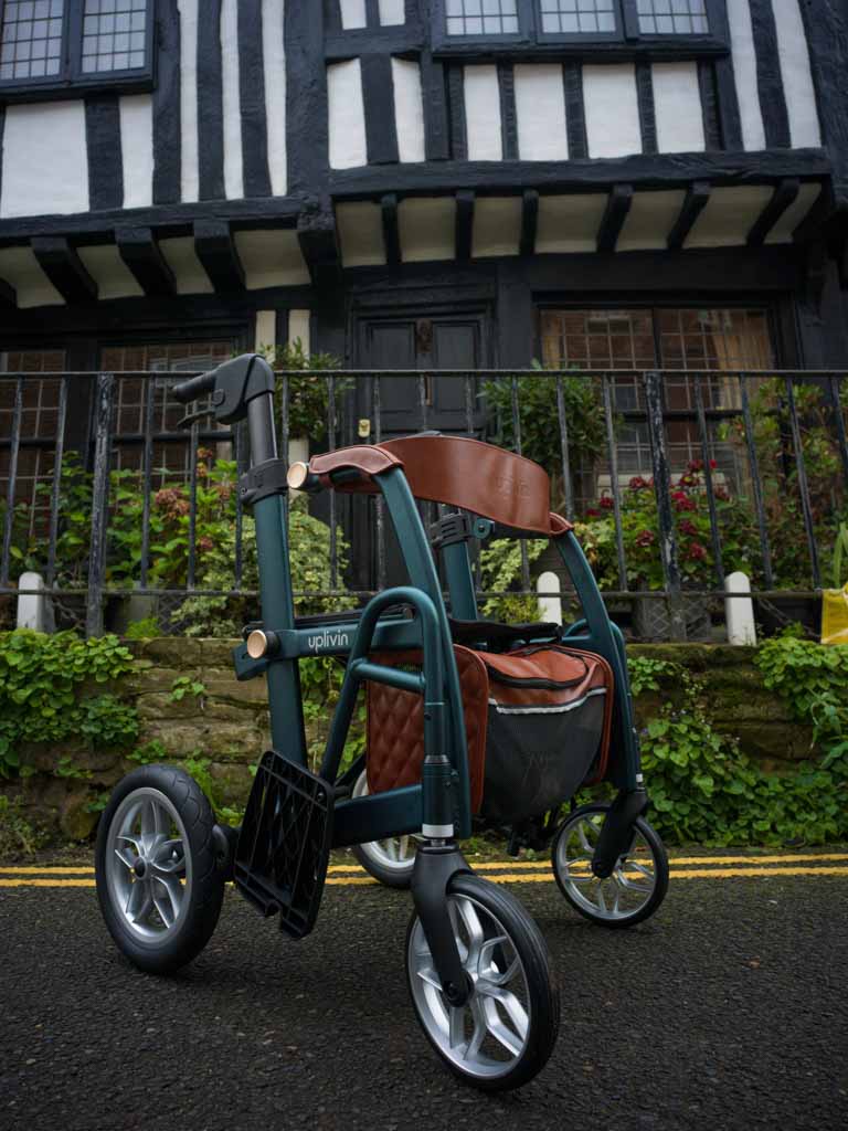 Green and brown walker wheelchair with a bag in front of a half-timbered building.