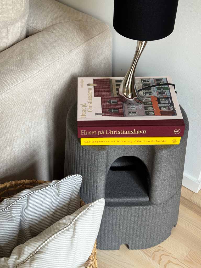 Grey Dorica stool with a book on top next to a lamp and sofa
