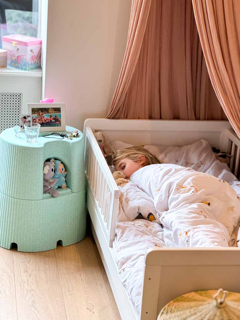 Child sleeping in a bed with a green stool next to them.