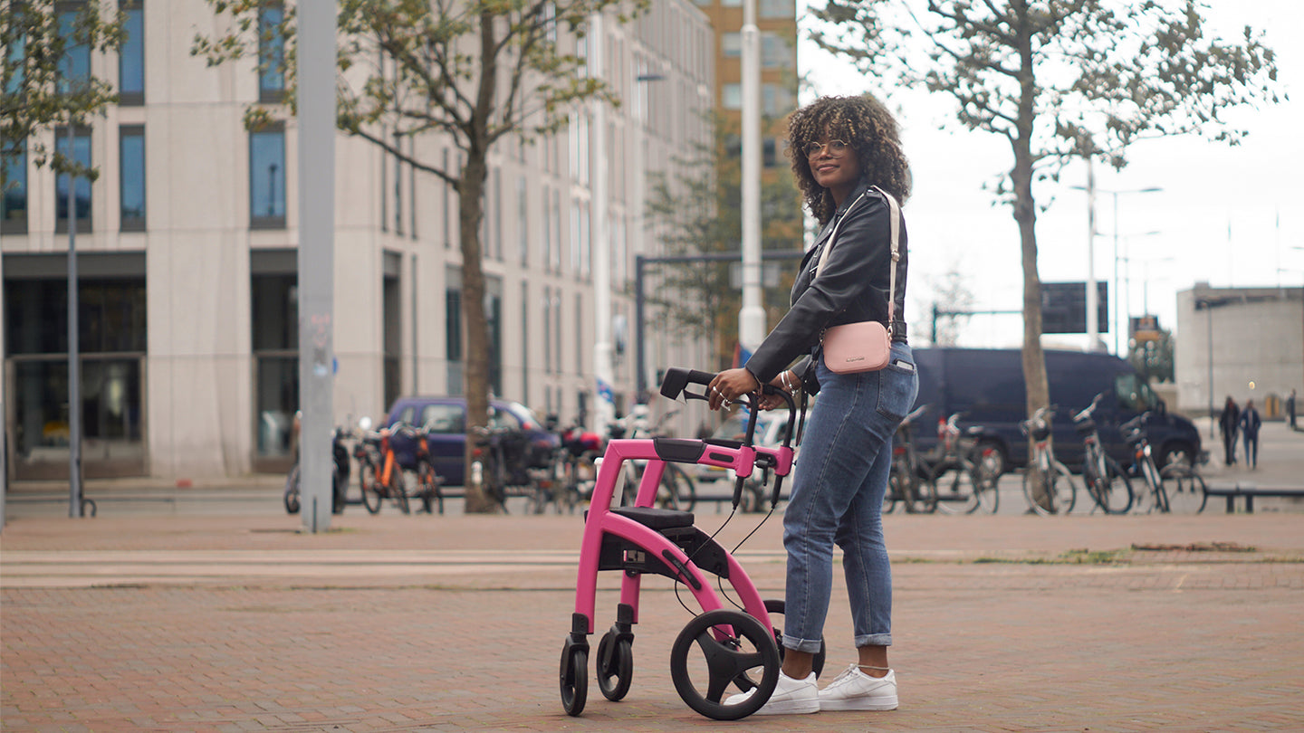 A woman stands using a Rollz Motion Walker Wheelchair for support with bikes and a building in the background