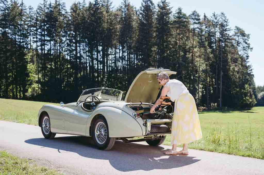 A woman puts her Saljol rollator into the boot of a sports car with trees and a grassy field in the background