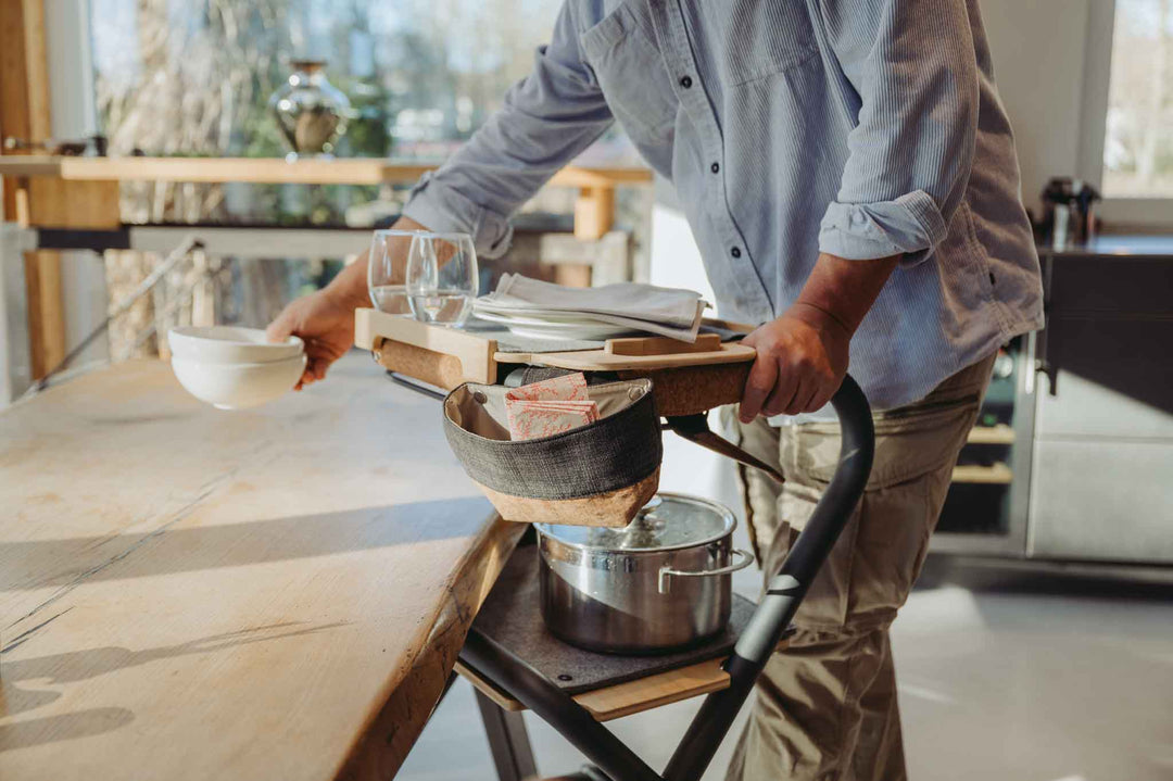 A person using a indoor mobility walker to bring glasses and bowls to a table in a kitchen