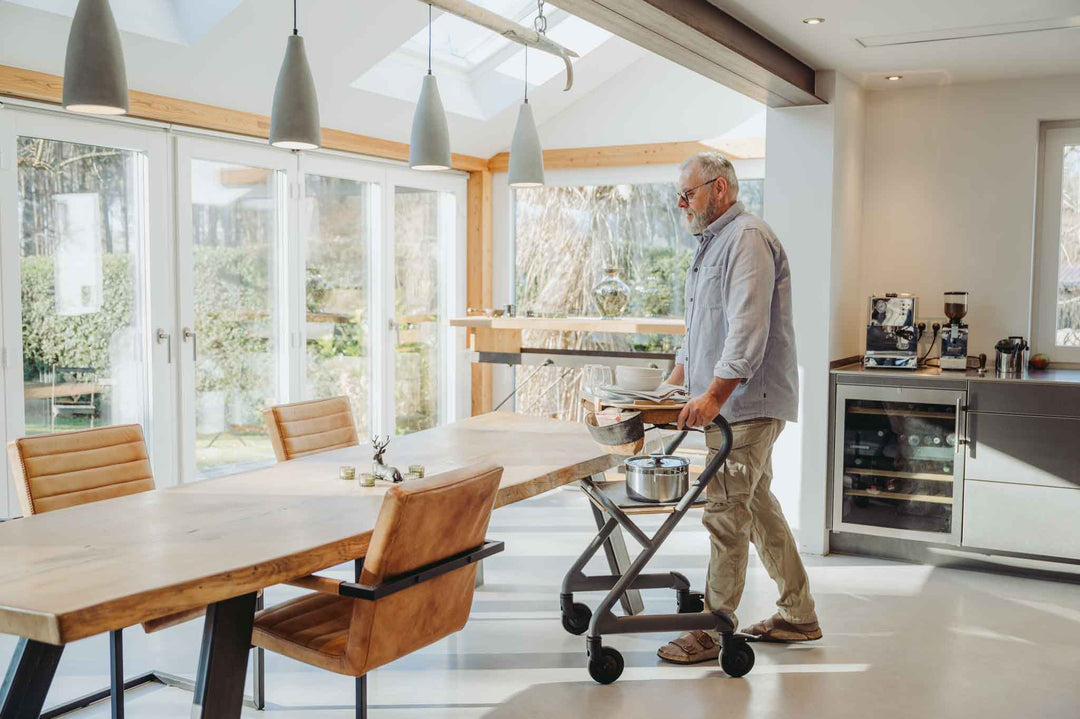 Man pushing a indoor mobility walker  with kitchen utensils in a modern kitchen with large windows
