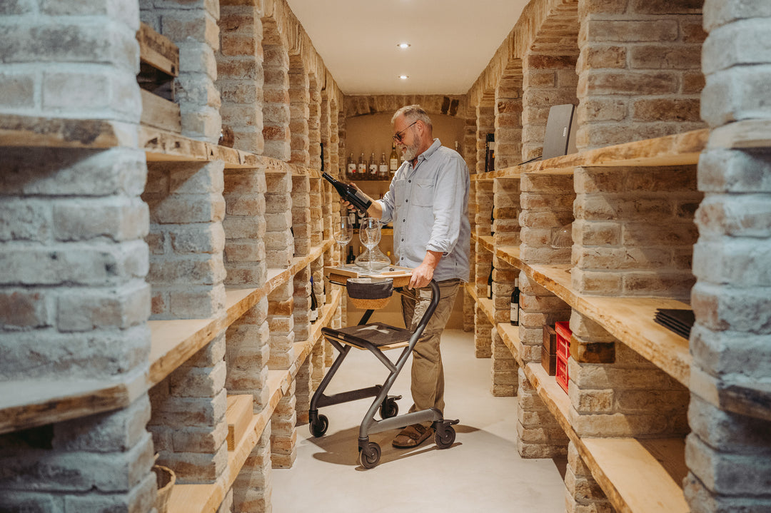 Man using a cart in a wine cellar with stone walls and wooden shelves.