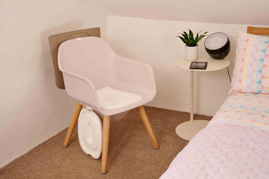 Stylish  commode chair with a small round table and plant in a bedroom setting.