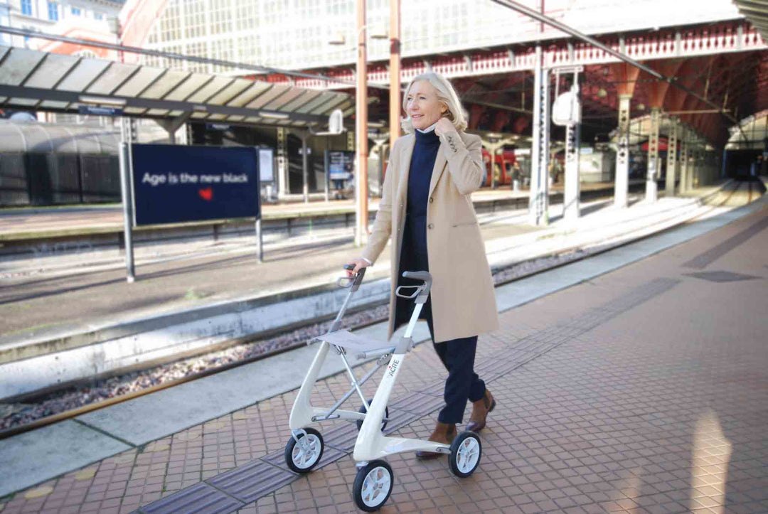 A woman walks along a platform at a train station using a lightweight walking frame