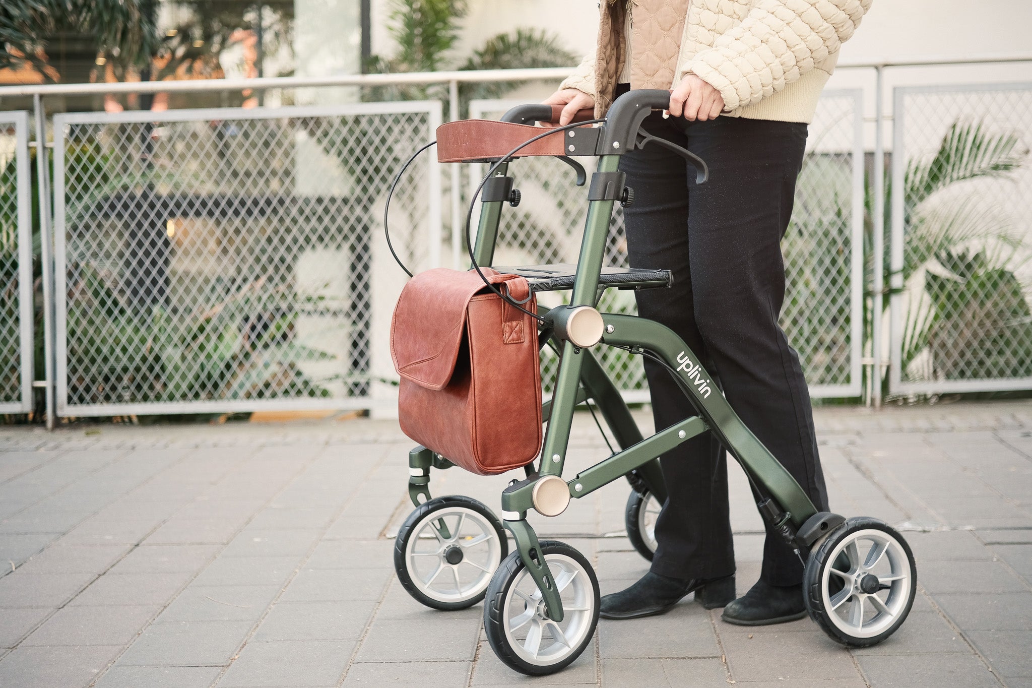 Close up of someone using the green 'Uplivin Trive' rollator on a brick footpath.