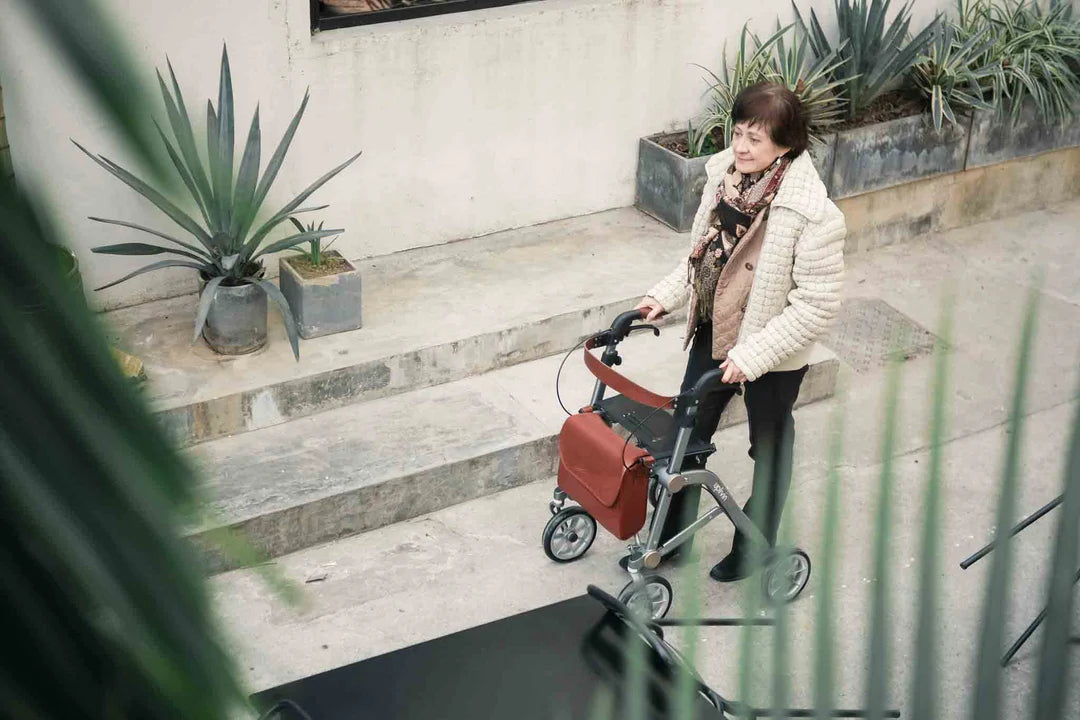 Woman pushing a red stroller with a white jacket and black pants, surrounded by plants.