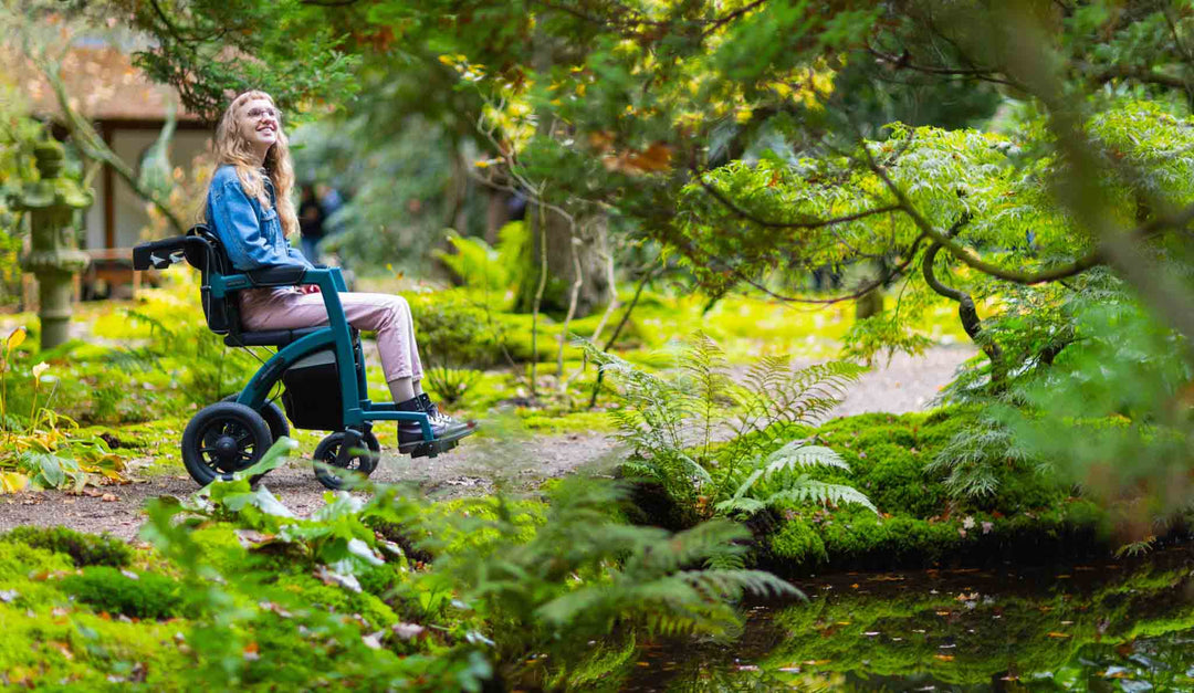 A smiling girl sits in a 'Rollz Motion Performance' wheelchair in a park with trees