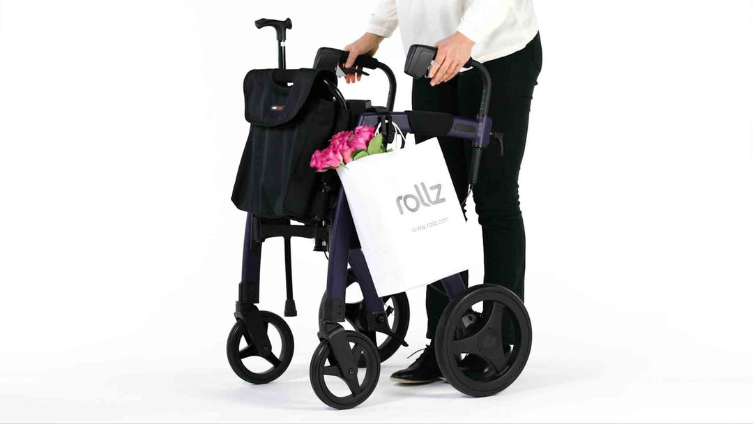 A Rollz Motion walking frame with a walking stick and a shopping bag attached